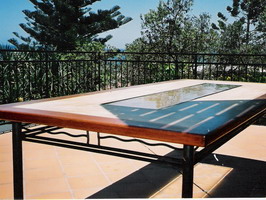 Custom table with kwela edge, sand finish panel, 318 stainless steel and slump glass panel on wrought iron base