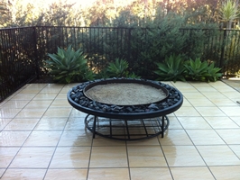 large japanese style fire pit on steel frame, black scoria lava stone finish, with lower wood rack